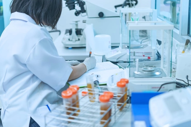 Scientist writing notes in a laboratory with test tubes and equipment around