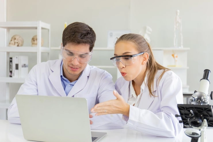 Two scientists discussing while looking at a laptop in a lab